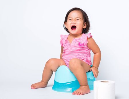Asian little cute baby child girl education training to sitting on blue chamber pot or potty with toilet paper rolls, studio shot isolated on white background, wc toilet conceptの写真素材