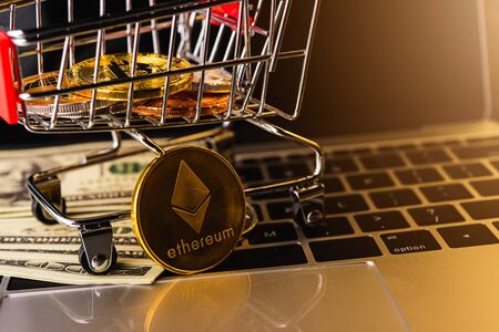 Shopping cart with golden ether coins or Ethereum network exchange and 100 dollars on keyboard of laptop computer, electronic money, blockchain and money cryptocurrency (crypto currency) conceptの写真素材