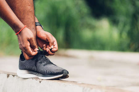 Close up Asian sport runner black man wear watch stand step on the footpath trying shoelace running...