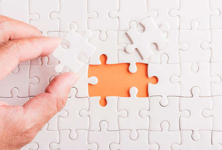 Top view flat lay of hand-holding last piece white paper jigsaw puzzle game last pieces put to place for solve problem complete mission, studio shot on an orange background, quiz calculation conceptの写真素材