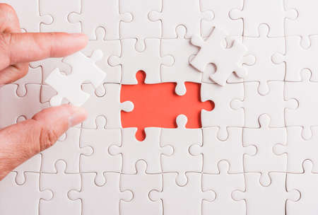 Top view flat lay of hand-holding last piece white paper jigsaw puzzle game last pieces put to place for solve problem complete mission, studio shot on a pink background, quiz calculation conceptの写真素材