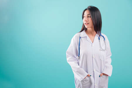 Asian doctor, happy beautiful young woman in uniform standing arms crossed, smiling with stethoscope looking out on blue background with copy space for text Medical health care staff service conceptの写真素材
