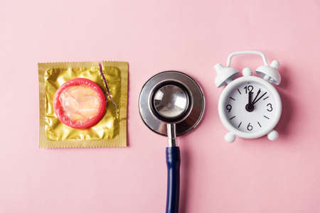 World sexual health or Aids day, Top view flat lay medical equipment, condom in a pack, stethoscope and alarm clock, studio shot isolated on a pink background, Safe sex and reproductive health conceptの写真素材