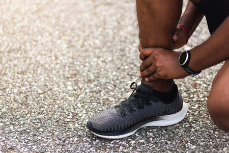 Close up Asian young sport runner black man wear watch hands joint hold leg pain because of twisted...