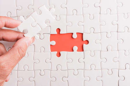 Top view flat lay of hand-holding last piece white paper jigsaw puzzle game last pieces put to place for solve problem complete mission, studio shot on a pink background, quiz calculation conceptの写真素材