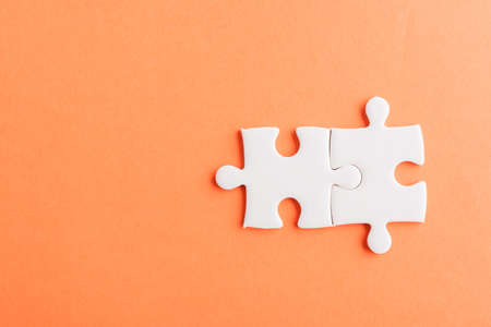 Top view flat lay of two paper plain white jigsaw puzzle game last pieces for solve, studio shot on an orange background, quiz calculation conceptの写真素材