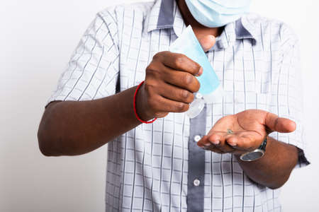 Closeup Asian black man wearing protective face mask  use sanitizer gel face clean his hand, hygiene prevention COVID-19 virus or coronavirus protection concept isolated on white backgroundの写真素材