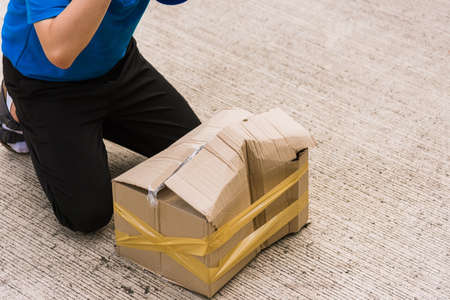 Asian young delivery man in blue uniform he emotional falling courier hold damaged cardboard box is...