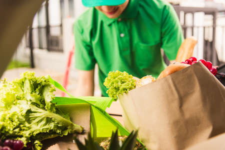 Asian delivery man grocery prepare service giving fresh vegetables food and fruit full in wooden basket on back car to send woman customer at door home after pandemic coronavirus, Back to new normalの写真素材