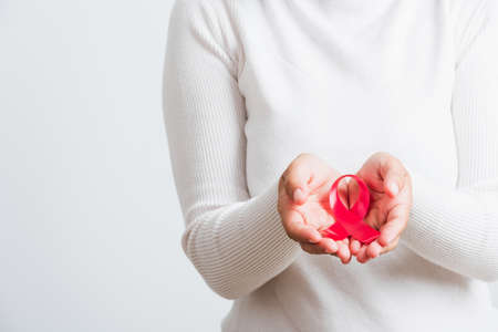 Breast cancer awareness healthcare and medicine concept. Close up Asian woman holding pink breast cancer awareness ribbon on hands treatment charity, studio shot isolated on white backgroundの写真素材