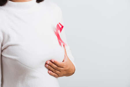 Breast cancer awareness healthcare and medicine concept. Close up Asian woman wear t-shirt she have pink breast cancer awareness ribbon on chest she hold breast by hand, isolated on white backgroundの写真素材