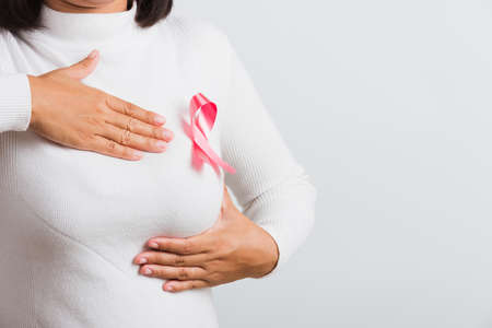 Breast cancer awareness healthcare and medicine concept. Close up Asian woman wear t-shirt she have pink breast cancer awareness ribbon on chest she hold breast by hand, isolated on white backgroundの写真素材