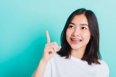 Portrait of Asian teen beautiful young woman smile have dental braces on teeth laughing point finger side away blank copy space, studio shot isolated on blue background, medicine and dentistry conceptの写真素材