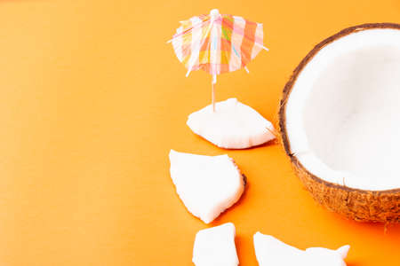 Happy coconuts day concept, fresh coconut pieces slices and sun umbrella, studio shot isolated on orange background, Beach tropical fruit spring summer holidayの写真素材