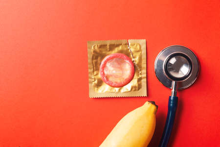 World sexual health or Aids day, Top view flat lay condom in wrapper pack, banana and doctor stethoscope, studio shot isolated on a red background, Safe sex and reproductive health conceptの写真素材