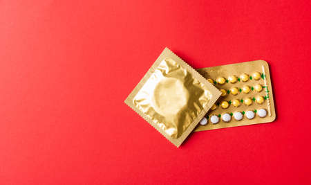 World sexual health or Aids day, condom on wrapper pack and contraceptive pills blister hormonal birth control pills, studio shot isolated on a red background, Safe sex and reproductive health conceptの写真素材