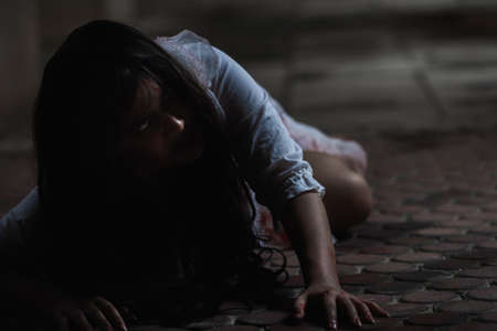 Girl zombie in blood. Asian Woman ghost with blood. Horror scary fear in dark house creepy crawling move slowly creeping out. Hair covering face her eye looking to camera, Halloween festival conceptの写真素材