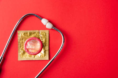 World sexual health or Aids day, Top view flat lay medical equipment, condom in pack and stethoscope, studio shot isolated on a red  background, Safe sex and reproductive health conceptの写真素材