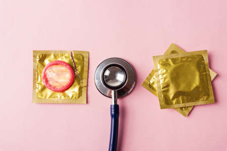 World sexual health or Aids day, Top view flat lay medical equipment, condom in pack and stethoscope, studio shot isolated on a pink background, Safe sex and reproductive health conceptの写真素材