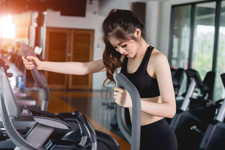 Young woman lifestyle using machine elliptical for cardio workout at fitness gym