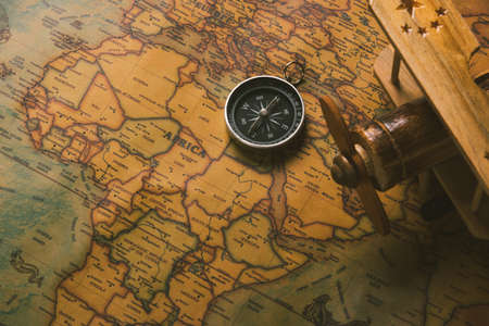 Old compass discovery and wooden plane on vintage paper antique world map background, Retro style cartography travel geography navigationの写真素材
