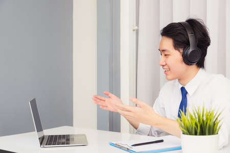 Work from home, Asian young businessman smile wearing headphones and suit video conference call or...