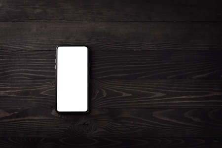 Close up top view of a modern smartphone on black wood table background vintage texture with copy...