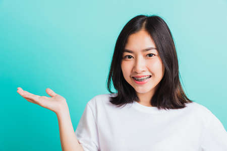 Portrait of Asian teen beautiful young woman smile have dental braces on teeth laughing she show hand side blank space, isolated on a blue background, Medicine and dentistry conceptの写真素材