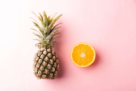 Close up above top view of ripe pineapple and orange fruit on pink pastel background, Summer...