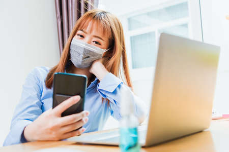 Asian young business woman wearing face mask protective using smart mobile phone for reading SMS...