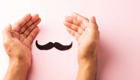 The man uses hand holding black mustache, studio shot isolated on white background, Prostate cancer awareness month, Fathers day, minimal November moustache conceptの写真素材