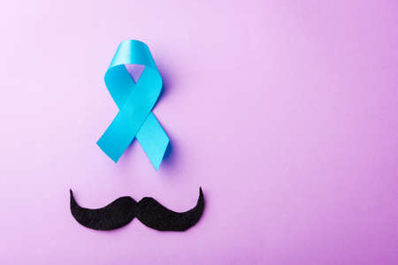 Black mustache paper and light blue ribbon, studio shot isolated on purple background, Prostate cancer awareness month, Fathers day, minimal November moustache conceptの写真素材