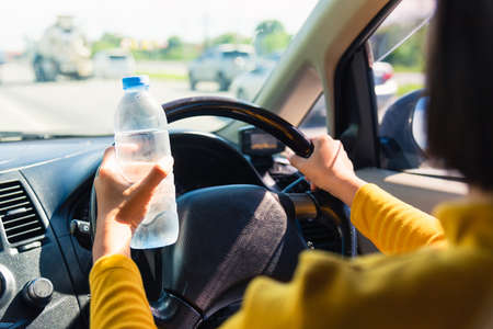 Asian woman holding a water bottle for drink while driving the car in the morning during going to work on highway road, Transportation and vehicle conceptの写真素材