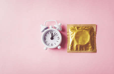 World sexual health or Aids day, condom in wrapper pack and Alarm clock birth control, studio shot isolated on a pink background, Safe sex and reproductive health conceptの写真素材