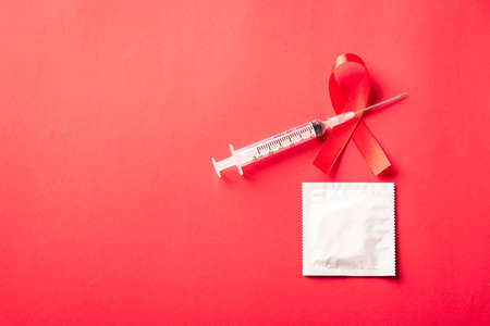 Red bow ribbon symbol HIV, AIDS cancer awareness, condom and syringe with shadows, studio shot isolated on red background, Healthcare medicine sexually concept, World AIDS Dayの写真素材