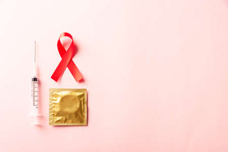 Red bow ribbon symbol HIV, AIDS cancer awareness, condom and syringe with shadows, studio shot isolated on pink background, Healthcare medicine sexually concept, World AIDS Dayの写真素材