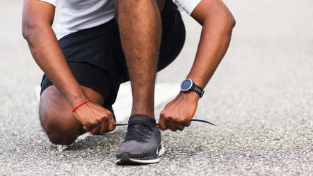 Close up Asian sport runner black man wear watch sitting he trying shoelace running shoes getting...