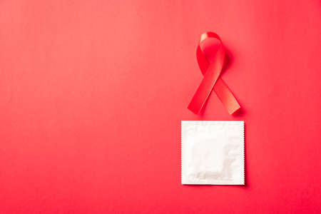 Red bow ribbon symbol HIV, AIDS cancer awareness and condom with shadows, studio shot isolated on red background, Healthcare medicine sexually concept, World AIDS Dayの写真素材