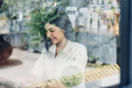 Freelance business woman working with laptop computer in coffee shop, View through clear glassの写真素材