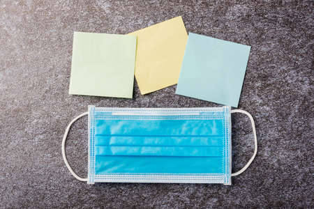 Above blank paper stick note list yellow, green and blue with the face mask protective on concrete...