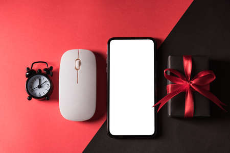 Black Friday sale shopping concept, Top view of gift box wrapped in black paper and black bow ribbon and modern mobile smartphone, studio shot on red and dark backgroundの写真素材