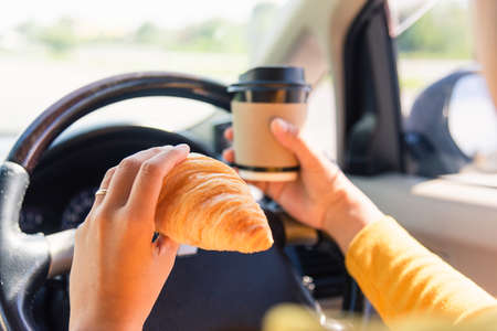 Asian woman eating food fastfood and drink coffee while driving the car in the morning during going to work on highway road, Transportation and vehicle conceptの写真素材