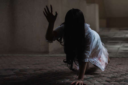 Female zombie in blood. Asian Woman ghost with blood. Horror scary fear in dark house creepy crawling move slowly creeping out. Hair covering face her eye looking camera, Halloween festival conceptの写真素材