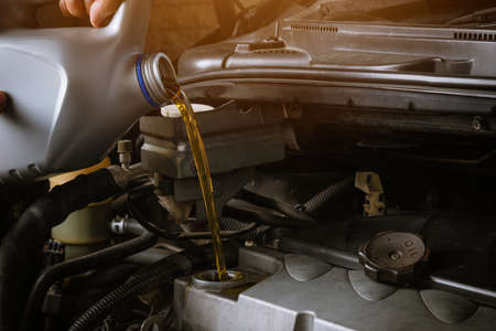 Mechanic in service to repair the car, refueling and pouring from bottle to change lubricant oil at...