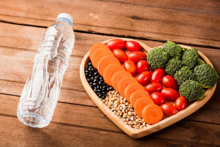 Top view of fresh organic fruits and vegetables in heart plate wood (carrot, Broccoli, tomato) and plastic water bottles on wooden table, Healthy lifestyle diet food conceptの写真素材