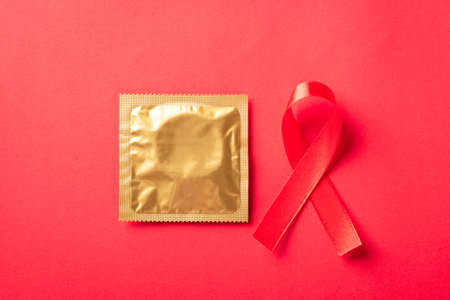 Red bow ribbon symbol HIV, AIDS cancer awareness and condom with shadows, studio shot isolated on red background, Healthcare medicine sexually concept, World AIDS Dayの写真素材