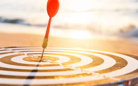 Dart arrow hit to center on bullseye(bull's-eye) of a dartboard is a target of purpose challenge business at sunset, expert strategy market target, objective financial and goal a conceptの写真素材