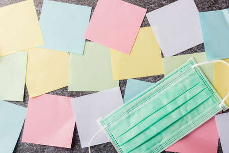 Above many blank paper stick note list with the face mask protective on concrete background,...