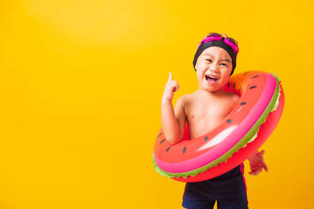Summer vacation concept, Portrait Asian happy cute little child boy wear goggles and swimsuit hold watermelon inflatable ring, Kid having fun on summer vacation, studio shot isolated yellow backgroundの写真素材