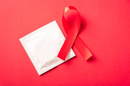 Red bow ribbon symbol HIV, AIDS cancer awareness and condom with shadows, studio shot isolated on red background, Healthcare medicine sexually concept, World AIDS Dayの写真素材